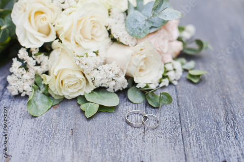 wedding rings and bouquet of white roses on wooden table © Dina