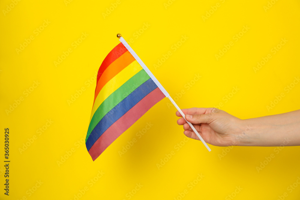 Female hand hold LGBT flag on yellow background Female hand hold LGBT flag on yellow background