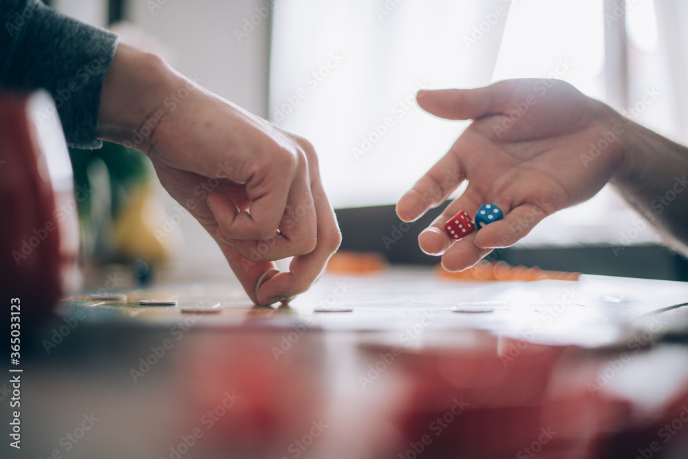 Board game and men's hands with chips and dice. The hand takes the chips, the other hand rolls the dice over the playing field Board game and men's hands with chips and dice. The hand takes the chips, the other hand rolls the dice over the playing field
