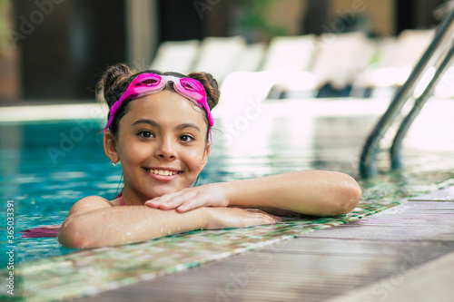 Happy beautiful little smiling girl in goggles and swimsuit in the pool has fun while vacationing or swimming lessons. © My Ocean studio