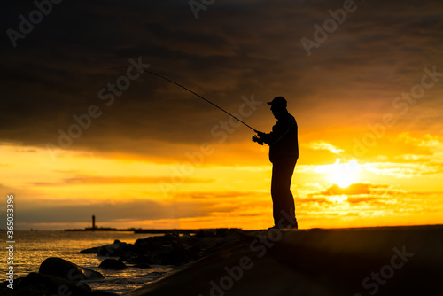 Silhouette of the fisherman on the pier during beautiful sunset © innervision
