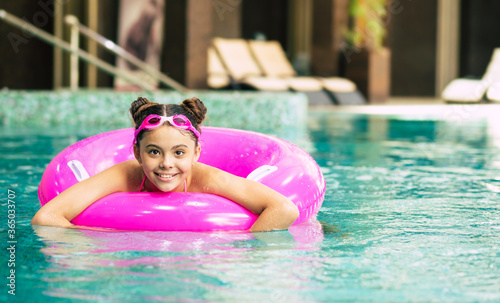 Happy little girl in goggles playing with a pink inflatable ring in the swimming pool on a hot summer day. Kids learn to swim. Child water toys.Family beach vacation.