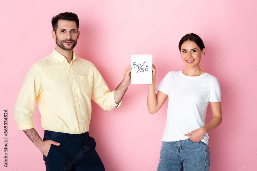 Φωτογραφία happy man and woman in white t-shirt holding paper with fifty-fifty symbols whil