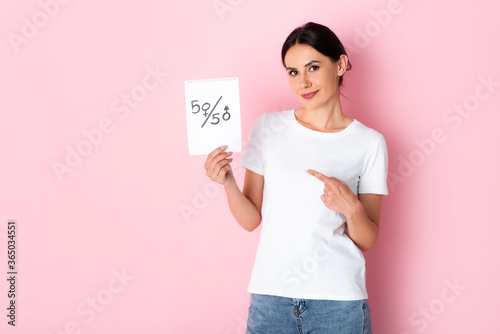 happy woman pointing with finger at paper with fifty-fifty symbols isolated on white, gender equality concept