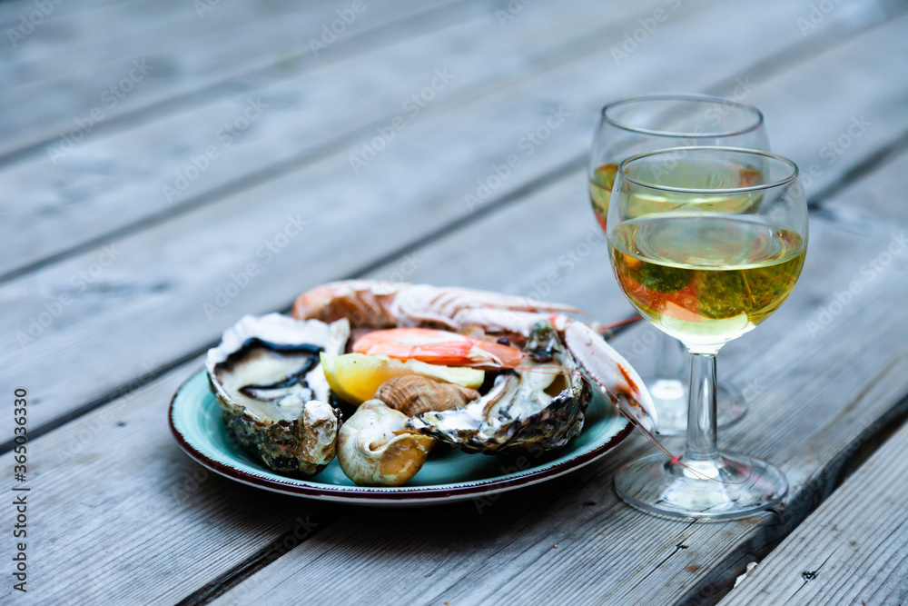 Delicious romantic gourmet lunch for two. Fresh raw oysters, shrimps, snails with glass of cold white wine. Perfect gormand lunch, traditional french appetizer. Wooden background, close up Delicious romantic gourmet lunch for two. Fresh raw oysters, shrimps, snails with glass of cold white wine. Perfect gormand lunch, traditional french appetizer. Wooden background, close up