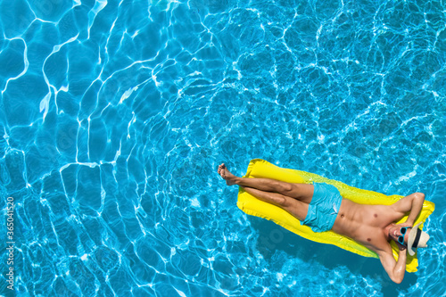 Young man with inflatable mattress in swimming pool, top view. Space for text