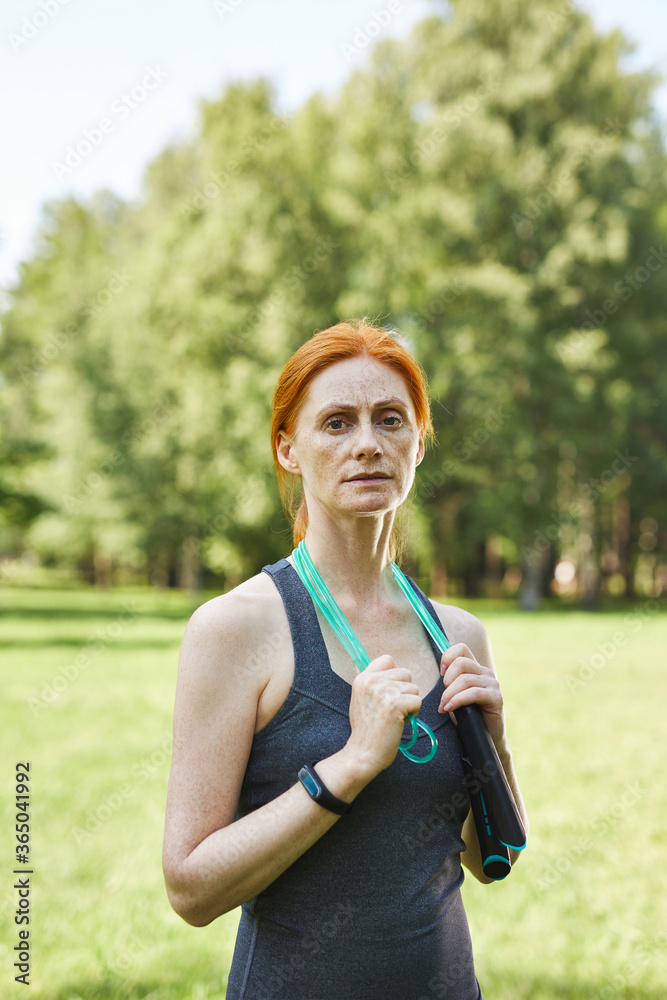 Portrait of serious fit mature woman holding jump rope around neck in beautiful park, fitness outside Portrait of serious fit mature woman holding jump rope around neck in beautiful park, fitness outside