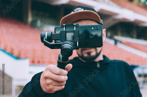 Blogger in the stadium shoots video on a smartphone with a manual camera stabilizer.