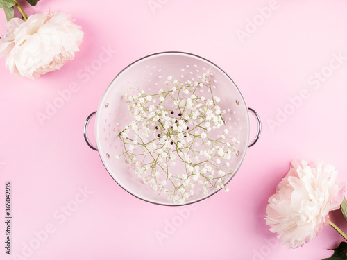 Pink colander with white flowers framed by peonies. Spring tableware concept