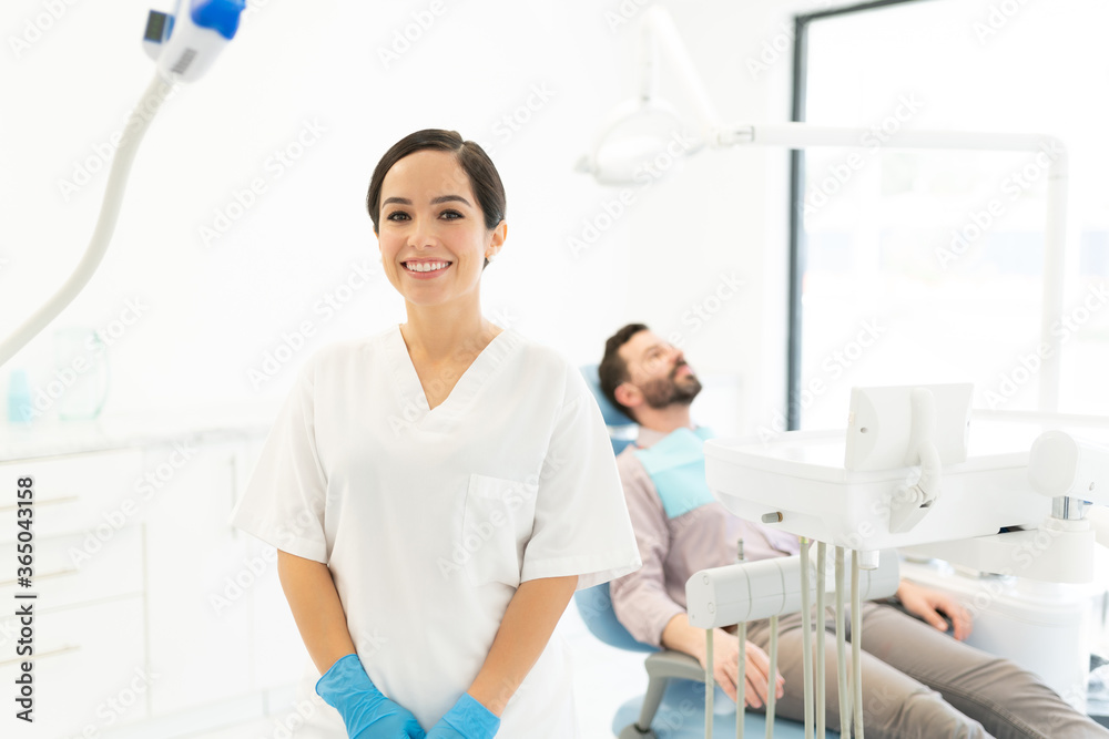 Smiling Dentist With Patient In Background Smiling Dentist With Patient In Background