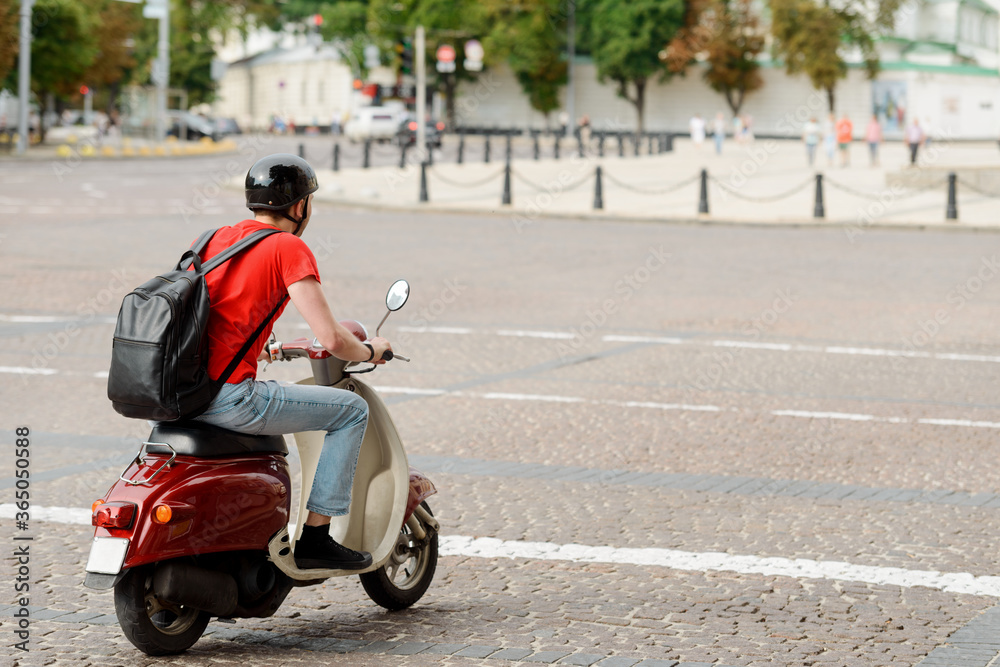 Man, with a backpack and helmet, is driving a scooter