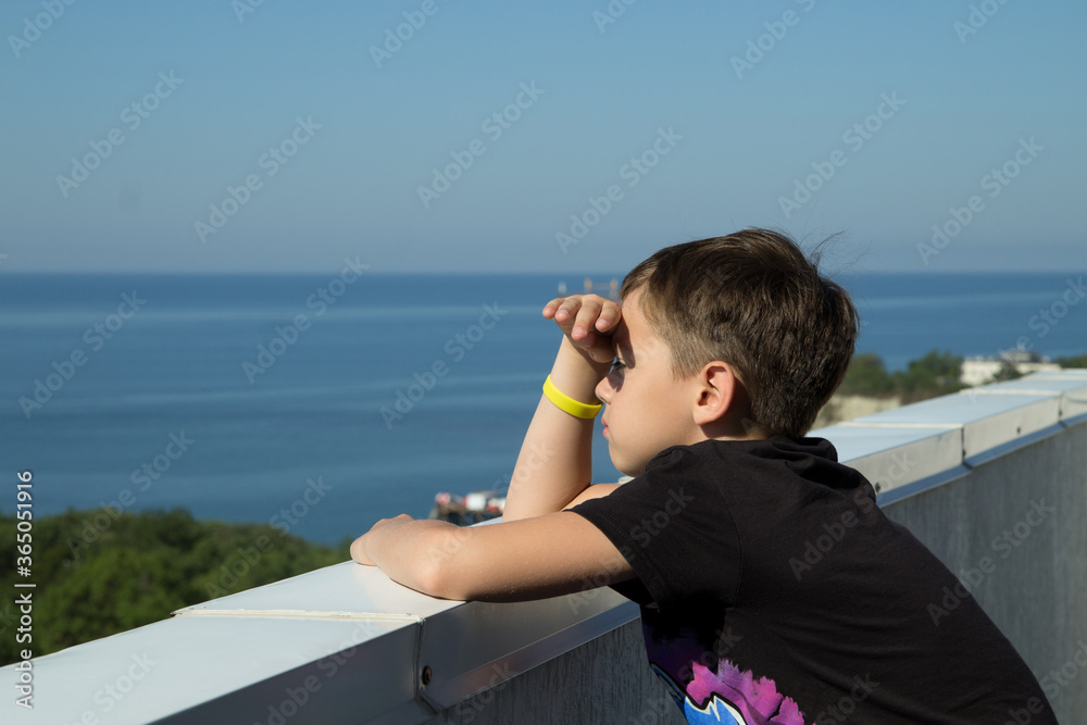 The boy sits on the roof of the house, looks sadly into the distance at sea. Expectation. The boy sits on the roof of the house, looks sadly into the distance at sea. Expectation.