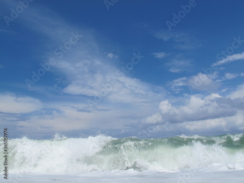  Waves at sea, tide, spray and foam in foreground, clear blue sky with white clouds. Summer vacation.