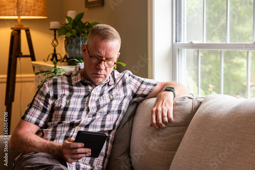 Mature man reading kindle on living room couch photo