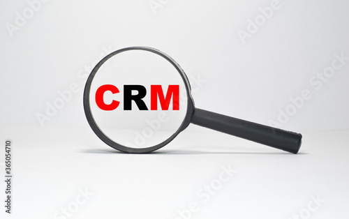 Red and black CRM inscription in a black magnifier on a white endless background