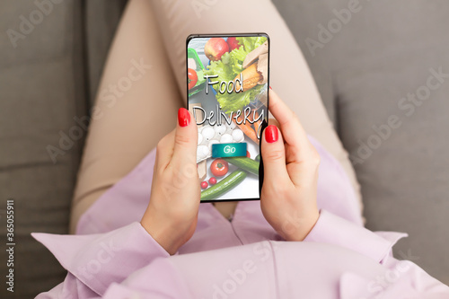 Girl ordering pizza online on smartphone, with table and coffee and plant in background