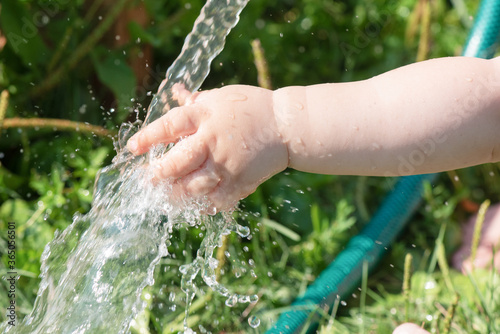 Little child is washing his hand under a water from a water hose in a garden.