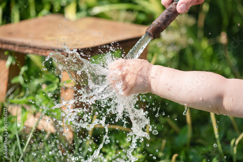 Little child is washing his hand under a water from a water hose in a garden.