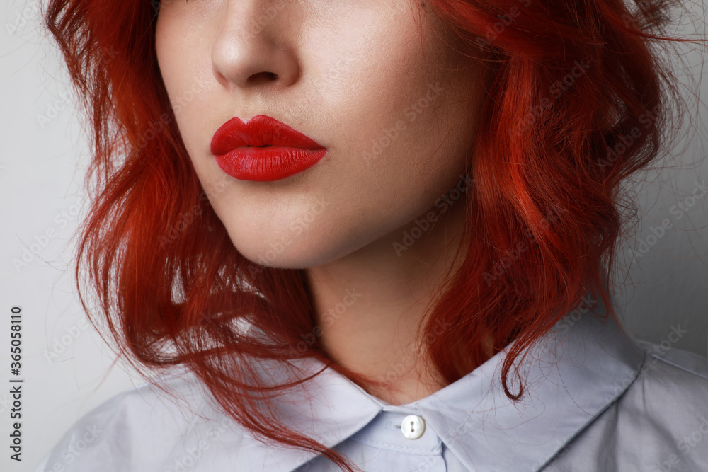 Close-up portrait of attractive young woman with long red hair, and bright make-up, posing over grey background. Close-up portrait of attractive young woman with long red hair, and bright make-up, posing over grey background.