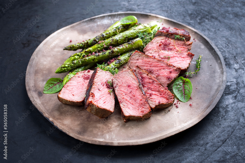 Barbecue dry aged wagyu roast beef steak with green asparagus and lettuce offered as close-up on a rustic modern design plate Barbecue dry aged wagyu roast beef steak with green asparagus and lettuce offered as close-up on a rustic modern design plate