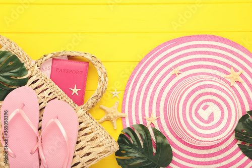 Summer straw hat with flip flops, monstera lefs, passport and starfishes on yellow wooden table photo