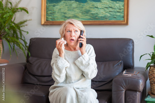 An elegant woman looks in surprise at the phone while sitting on a sofa in her house.