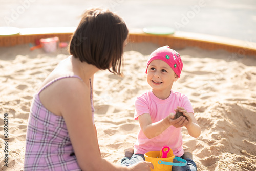 Small cute girl with mom share a sandcastle in a sandbox