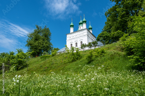 A snow-white church with green domes on the edge of a high cliff.