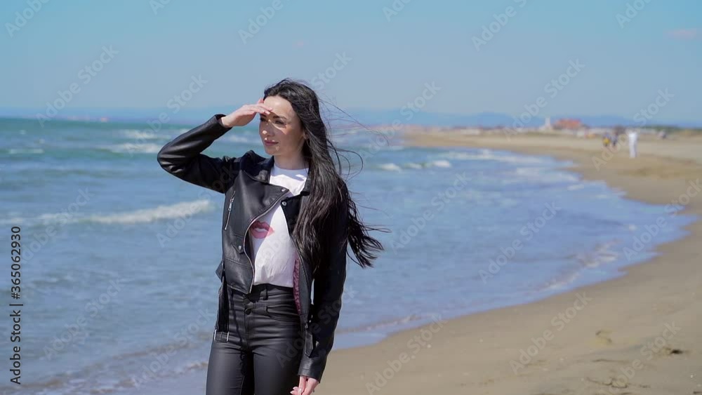 Portrait of a young stylish attractive girl walking or standing alone by the sea or ocean. Female with black hair in sunglasses sad dreams dreamy. The wind blows the hair. Beach. sea coast. Woman Portrait of a young stylish attractive girl walking or standing alone by the sea or ocean. Female with black hair in sunglasses sad dreams dreamy. The wind blows the hair. Beach. sea coast. Woman