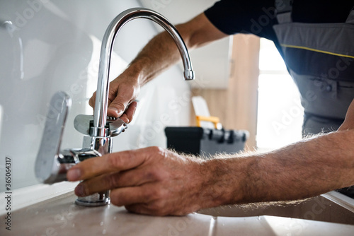 Close up of hands of aged repairman in uniform working, fixing broken kitchen tap using adjustable wrench. Repair service concept