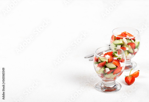 Berry and vegetable salad of strawberries and cucumber with feta cheese in a glass on a light background. 