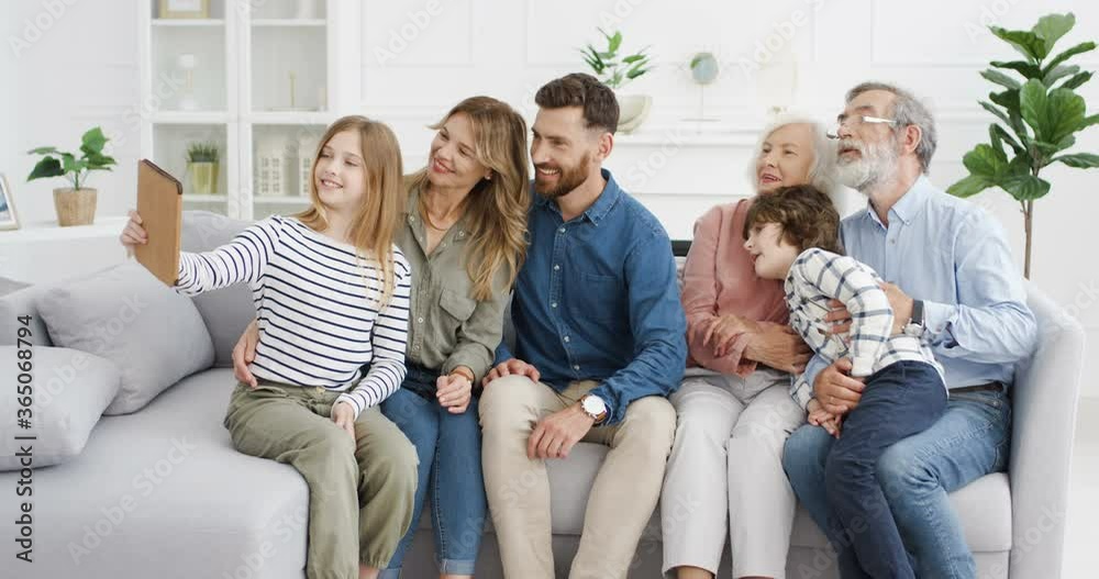 Caucasian family sitting on couch at home and taking selfie photo on tablet device. Kids with parents and grandparents making photos on computer. Old pensioners with children and grandchildren. Caucasian family sitting on couch at home and taking selfie photo on tablet device. Kids with parents and grandparents making photos on computer. Old pensioners with children and grandchildren.