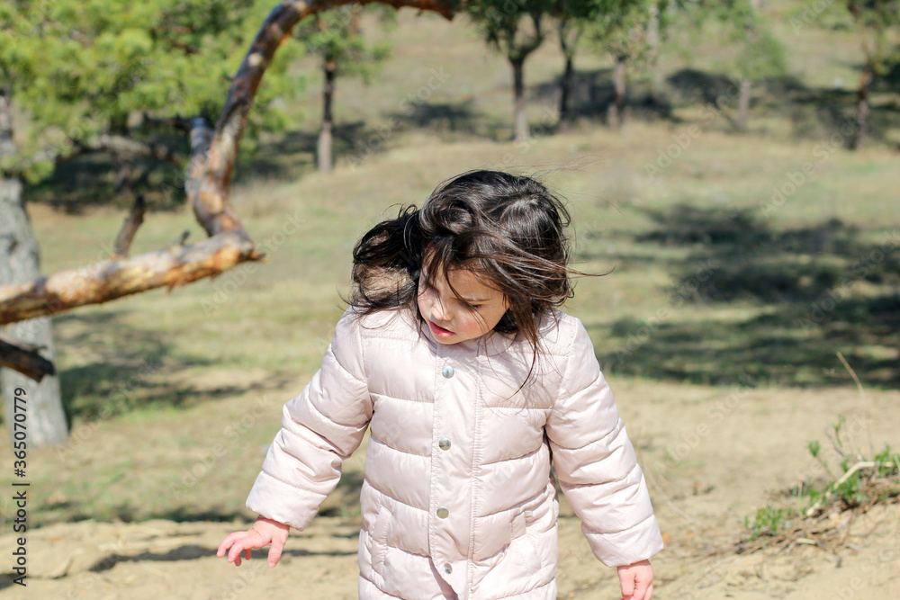 White girl preschooler with fluttering hair in a warm jacket rises uphill in the forest against a background of trees and grass White girl preschooler with fluttering hair in a warm jacket rises uphill in the forest against a background of trees and grass