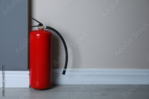 Fire extinguisher near light wall indoors. Space for text