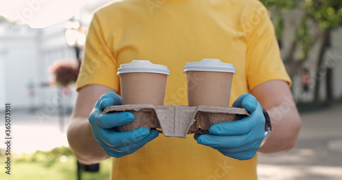 A close up of a man's hands in blue medical gloves holding a carry tray with two cups of morning fragrant coffee.