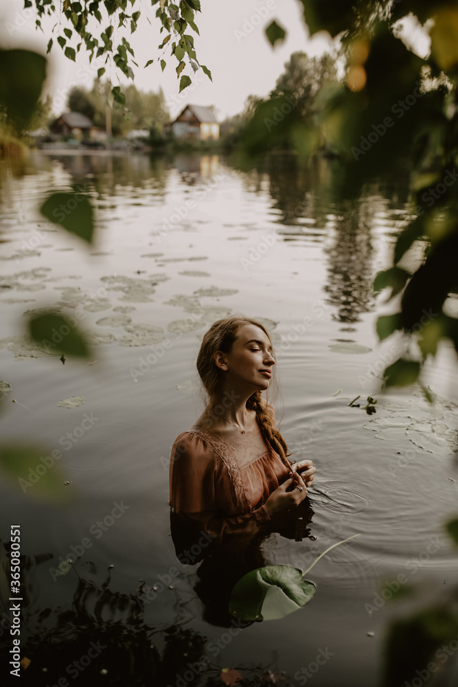 a beautiful young girl in a pink dress stands in a lake with water lilies