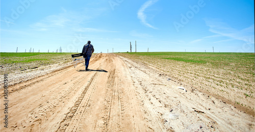 Lonely unmarked man with a production chair walks away on an old broken road