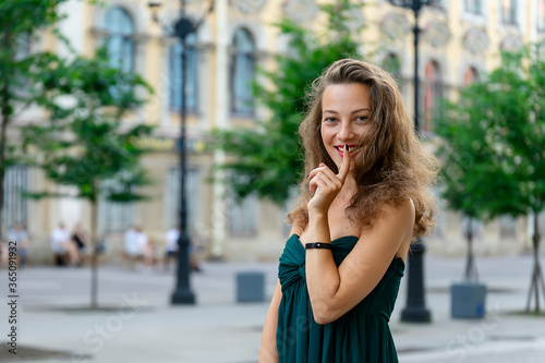 Beautiful girl in a green dress with bare shoulders posing smiling on a background of old buildings