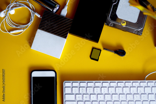 table with yellow background, several different hds, phone, screen, keyboard. Top view.   photo