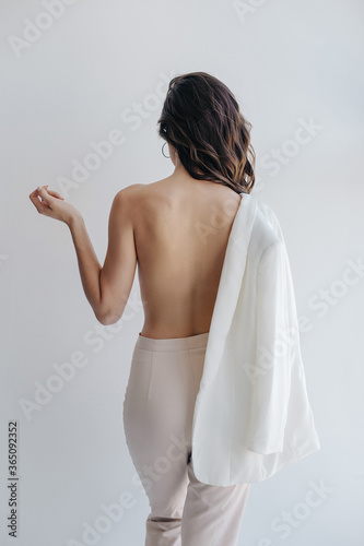 Girl with bare back, jacket on one shoulder and in trousers turned away from the camera and no face visible