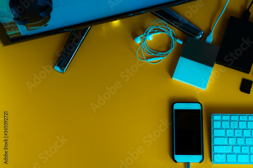 table with yellow background, several different hds, phone, screen, keyboard. Top view. photo