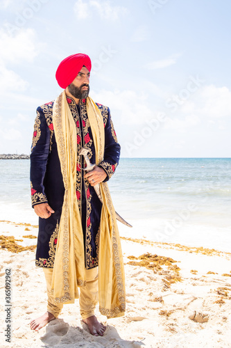 Attractive male Sikh model in traditional wedding attire on beach beneath sunny blue skies