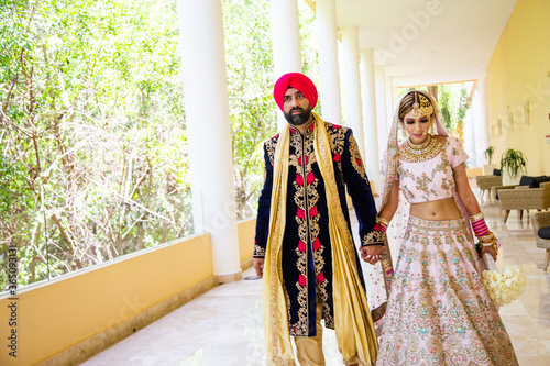 Sikh bride and groom wearing bright traditional clothing on clear sandy beach beneath sunny blue skies