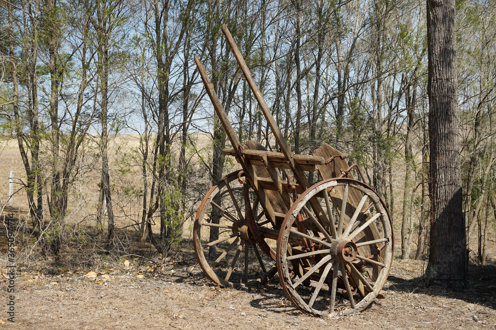 Old weathered wooden farm cart in a rural setting with trees and hill in the background. Queensland Australia 