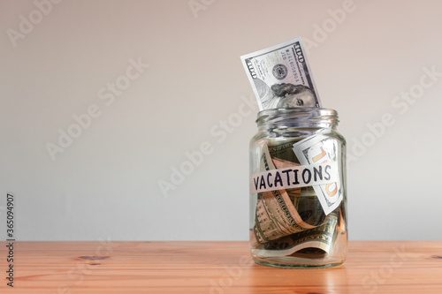 Money US Dollar bills in a glass jar labeled "vacations". Saving financial concept