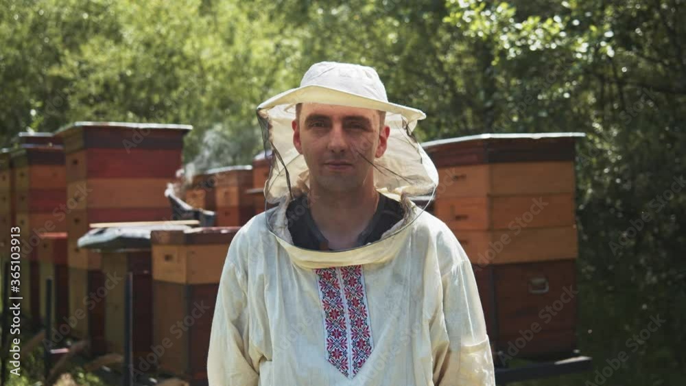 Positive caucasian apiarist in beekeeper protection looks at camera smiling on sunny day. Apiary farmer. Beemaster. Positive caucasian apiarist in beekeeper protection looks at camera smiling on sunny day. Apiary farmer. Beemaster.