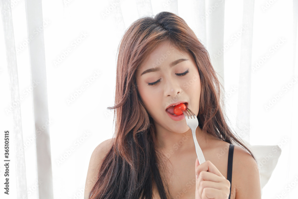 Portrait of a Asian sexy woman wear black bra or underwear and posing on white bed, spicy girl diet eating tomato fruit or vegetable Portrait of a Asian sexy woman wear black bra or underwear and posing on white bed, spicy girl diet eating tomato fruit or vegetable