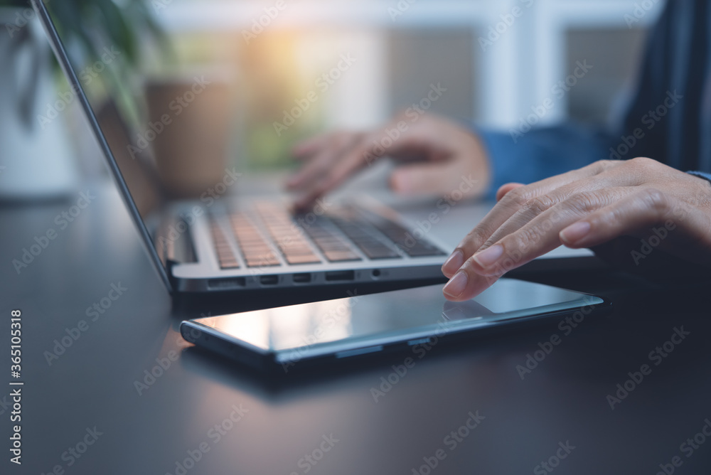 Close up of business woman using mobile phone while online working on laptop computer at home office Close up of business woman using mobile phone while online working on laptop computer at home office
