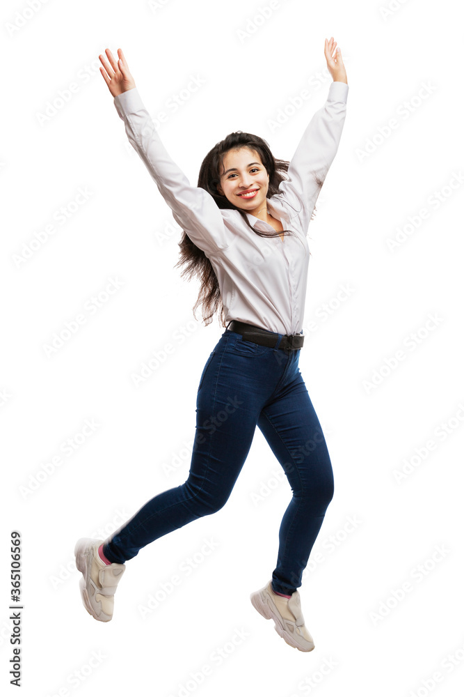 A young girl in jeans and a white shirt is jumping. Smiling brunette with long hair. Movement and energy. Isolated on a white background. Vertical. A young girl in jeans and a white shirt is jumping. Smiling brunette with long hair. Movement and energy. Isolated on a white background. Vertical.