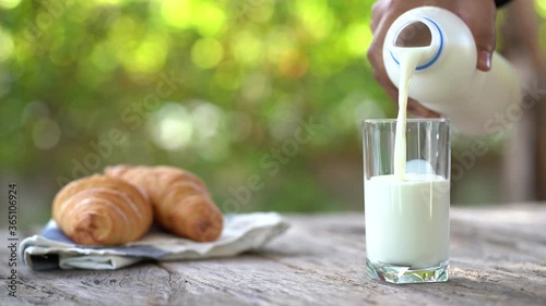 An empty glass and a bottle of milk stands on a wooden table. Girl's hand pours milk into a glass on a dark background.